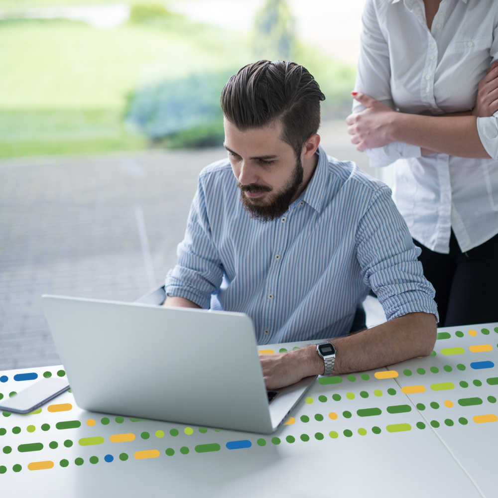 male looking at laptop with female stood behind