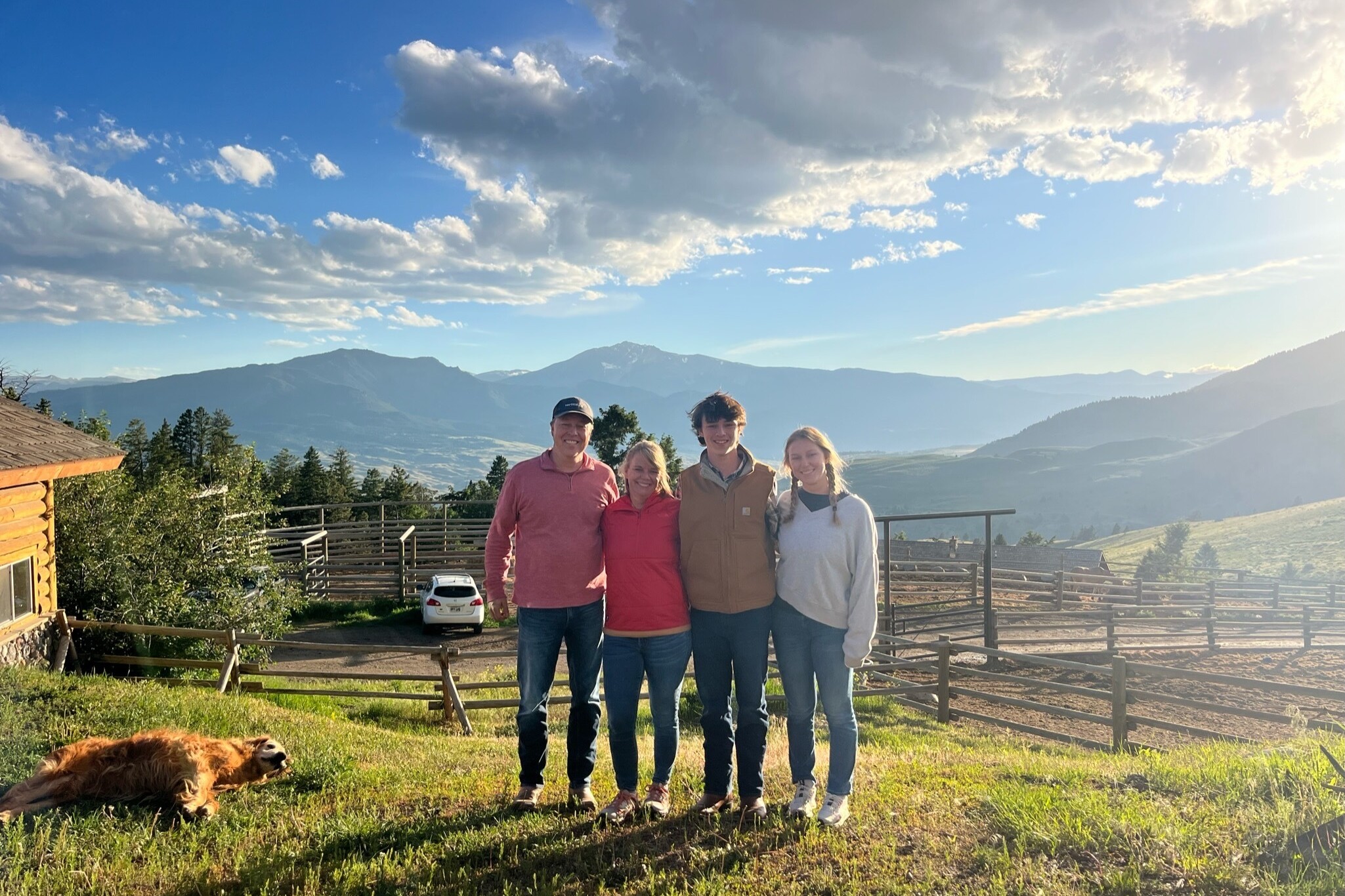 A family of four standing in front of the Montana mountains and a golden retriever laying in the corner