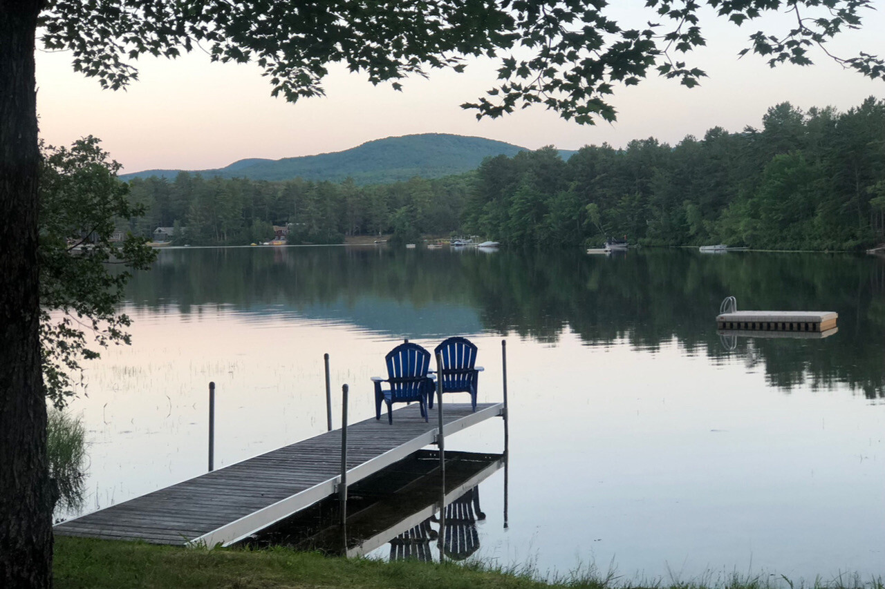 two chairs on a dock looking out towards a lake with mountains in the distance