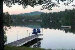 photo of two chairs on a dock looking out towards a lake with mountains in the distance
