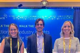 3 Vertical IQ employees stand in front of a bright blue background, smiling and excited to be at this banking conference.