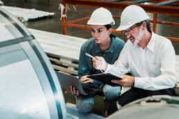 Two Machine Shop workers in a factory talking together with hard hats on.