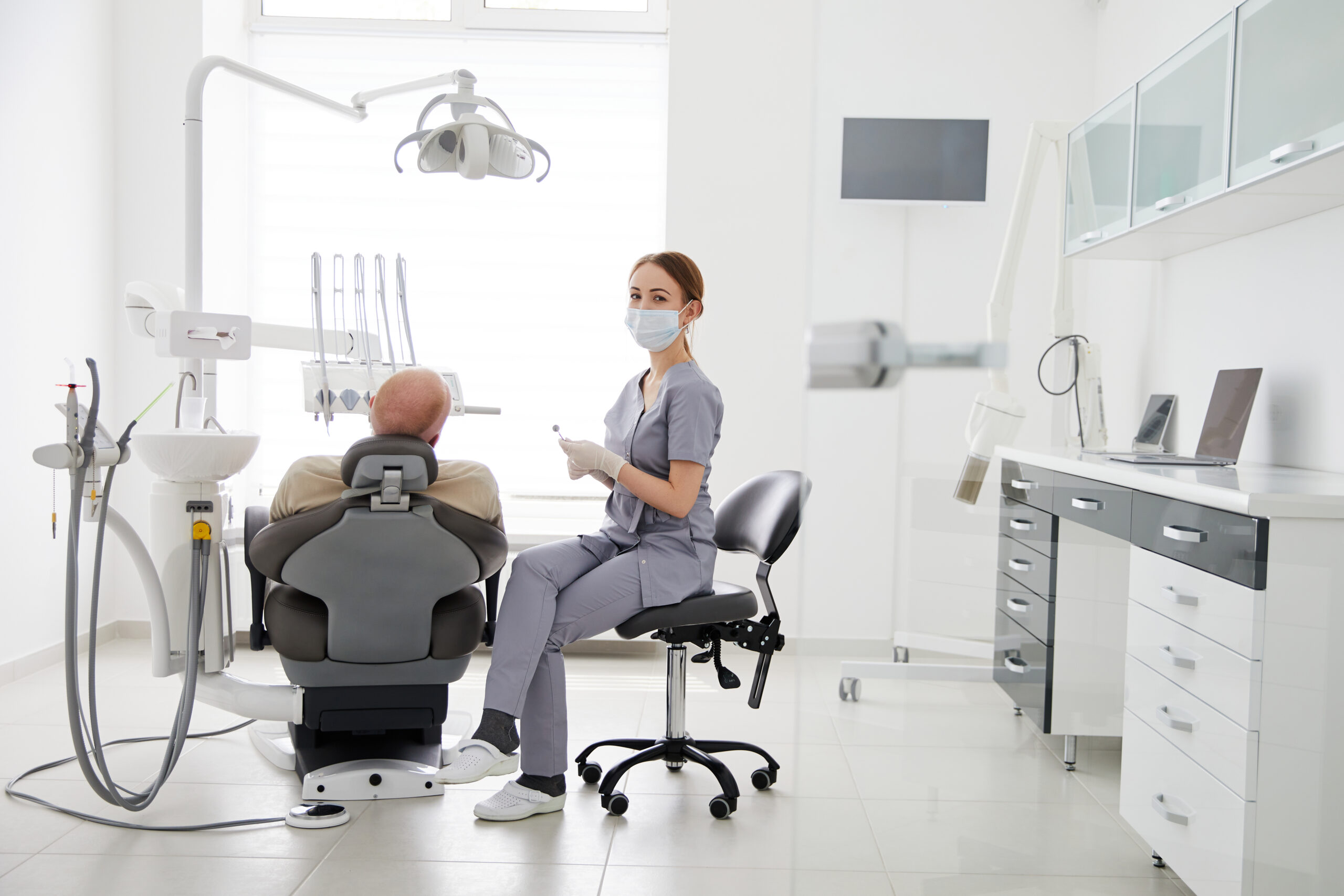 Portrait of young female dentist standing by mid adult man in clinic. Female dentist repairing patient tooth ; dental practices